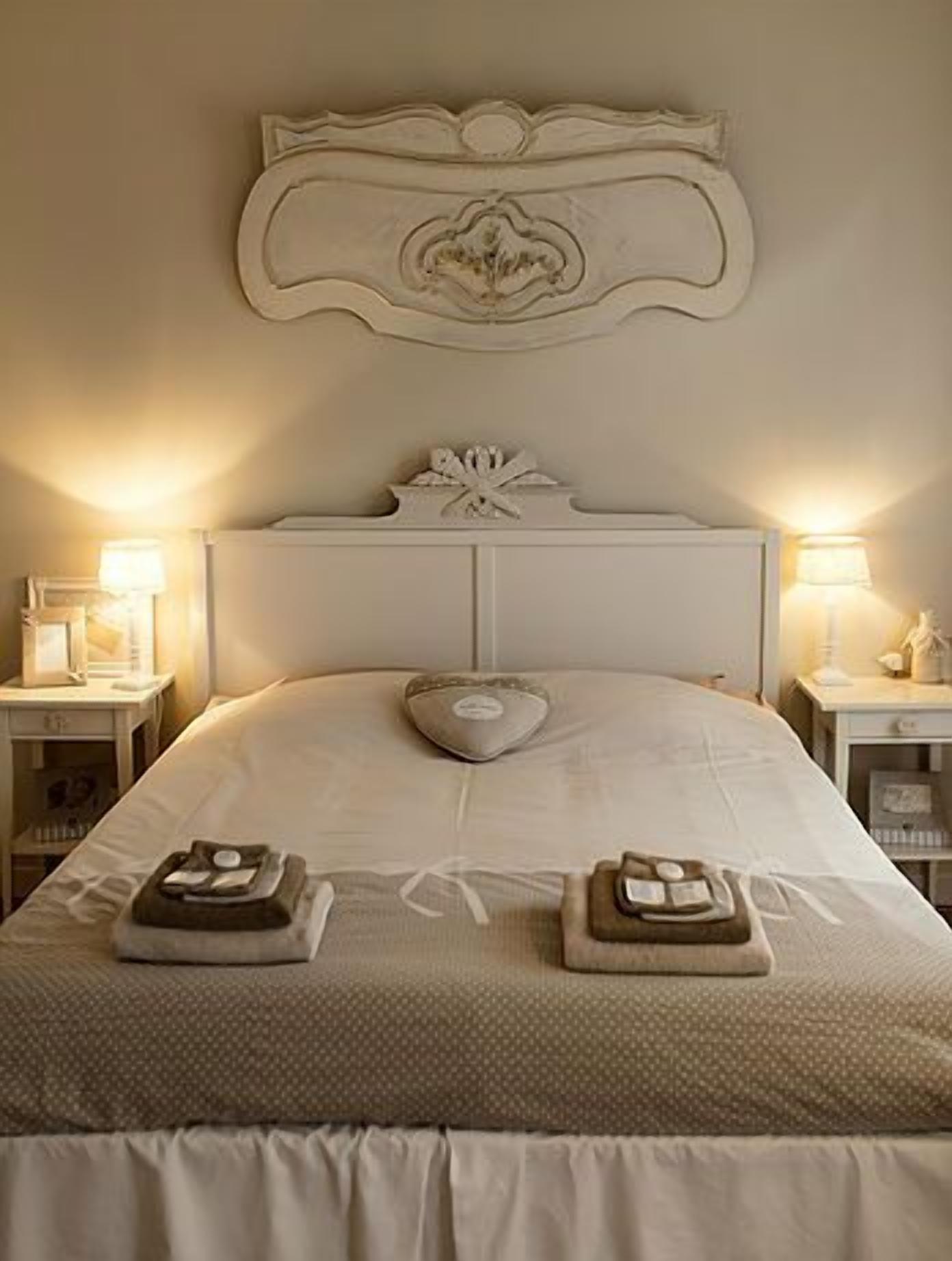A neatly made bed with a decorative headboard, two bedside tables with lamps, and a heart-shaped pillow.