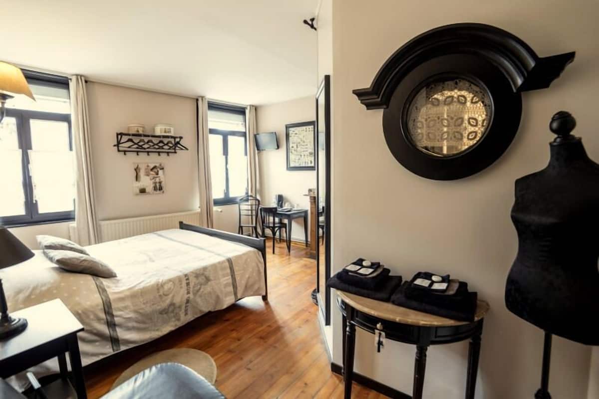 Een compacte slaapkamer met een bed, een bureau, een stoel en een ronde spiegel aan de muur.