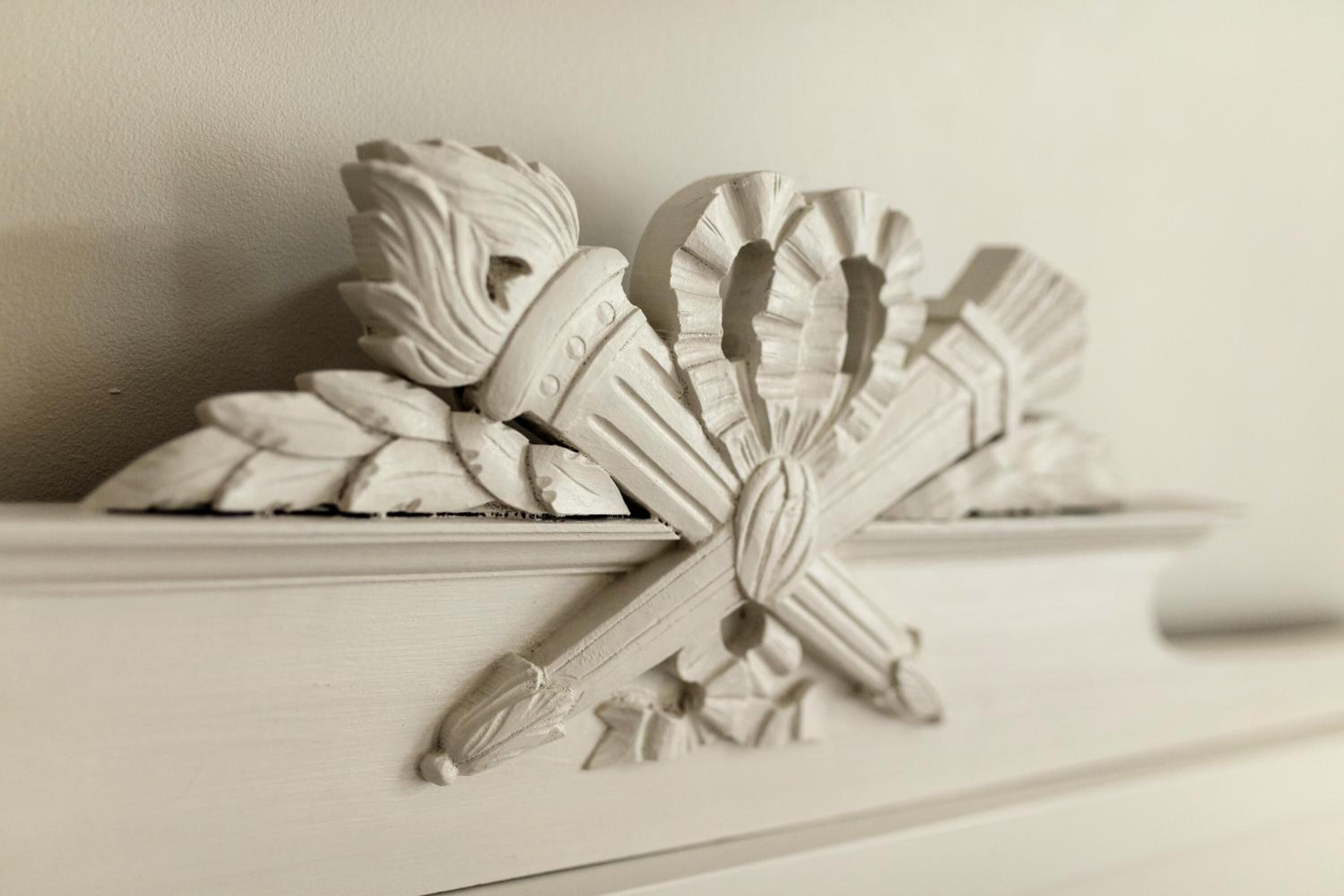 Un oggetto decorativo bianco con motivi floreali e a foglia su uno scaffale.