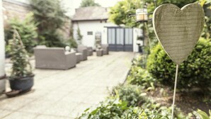 Un chemin de jardin mène à un bâtiment blanc agrémenté de meubles d’extérieur gris.
