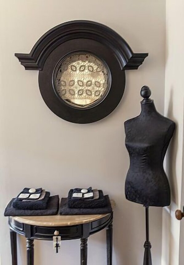 Un reloj de pared con esfera redonda y marco negro, un maniquí negro y una pequeña mesa con dos cojines negros.