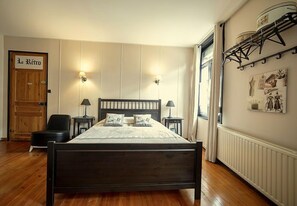 Een slaapkamer met een houten bed, twee bedlampen, een stoel, een radiator en een deur met de tekst 