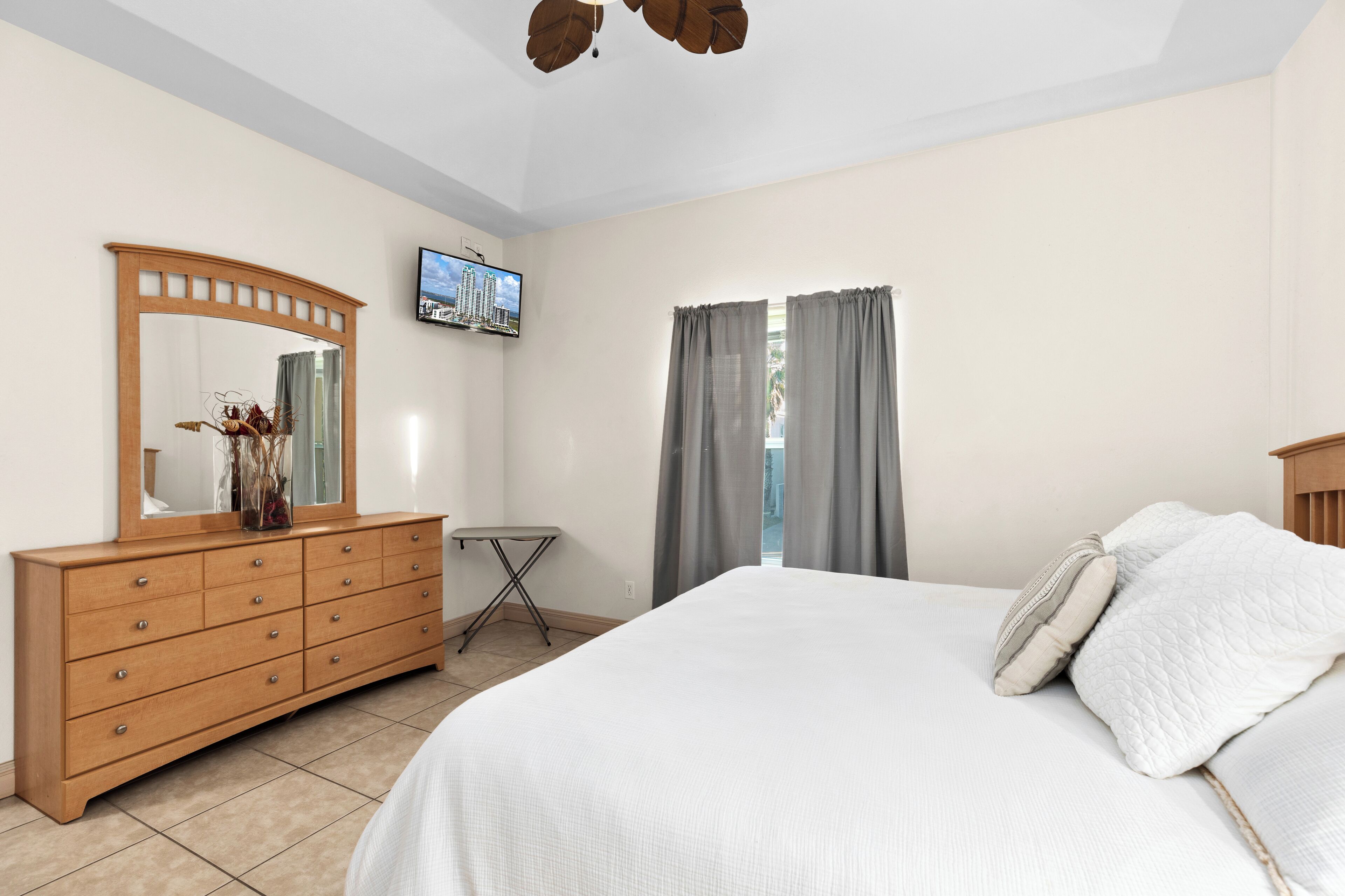 Une chambre à coucher avec un lit, une commode, un miroir, une télévision et des rideaux.