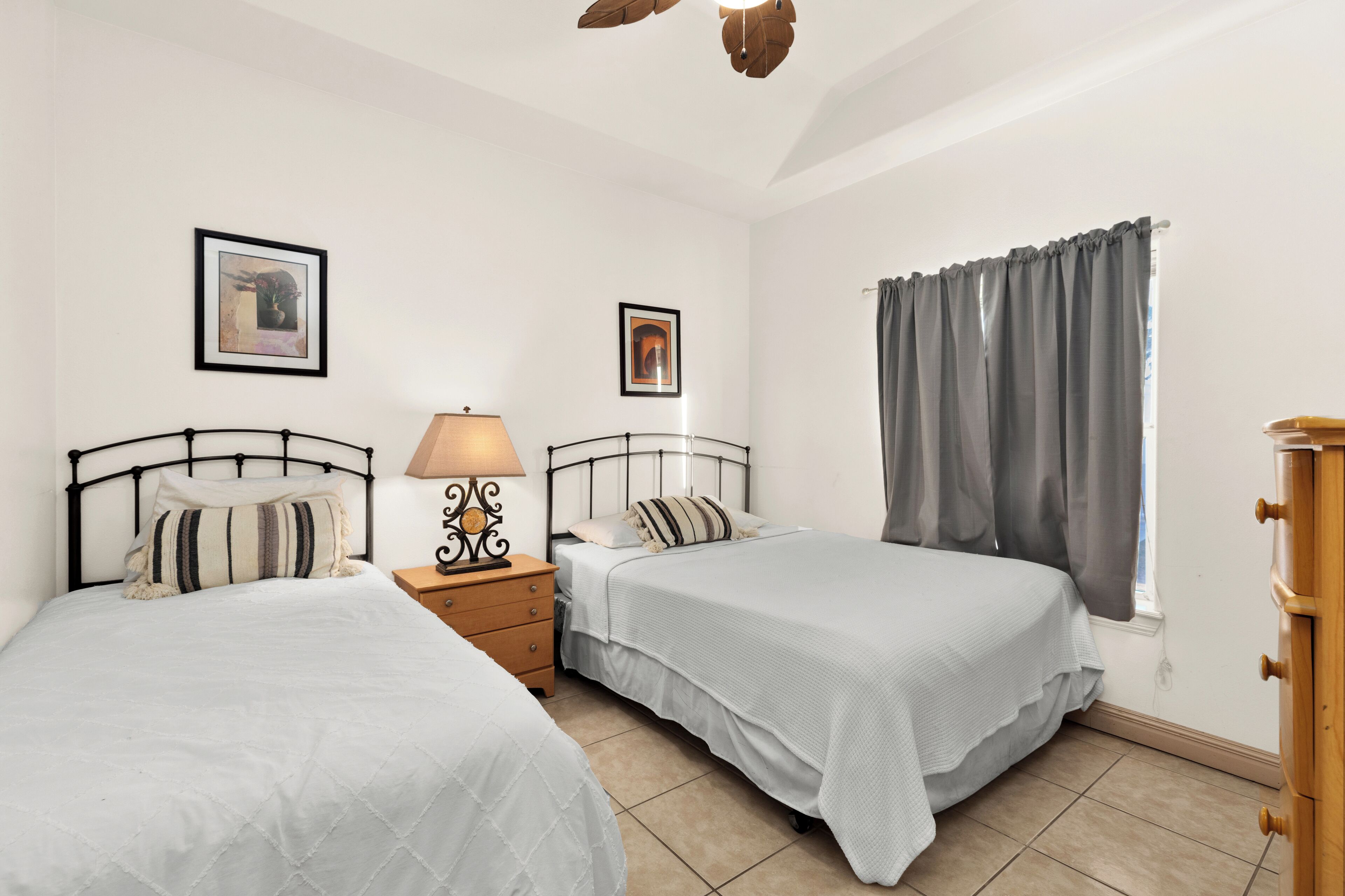 A bedroom with two beds, a nightstand with a lamp, and a dresser.