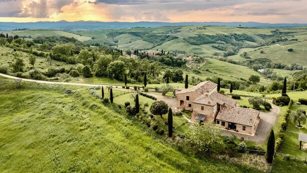 Un paysage rural avec des collines douces, une maison en pierre avec un toit de tuiles et un sentier sinueux.