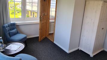 Una habitación con dos sillones azules, una mesita redonda, un armario blanco y una puerta que da a un balcón.