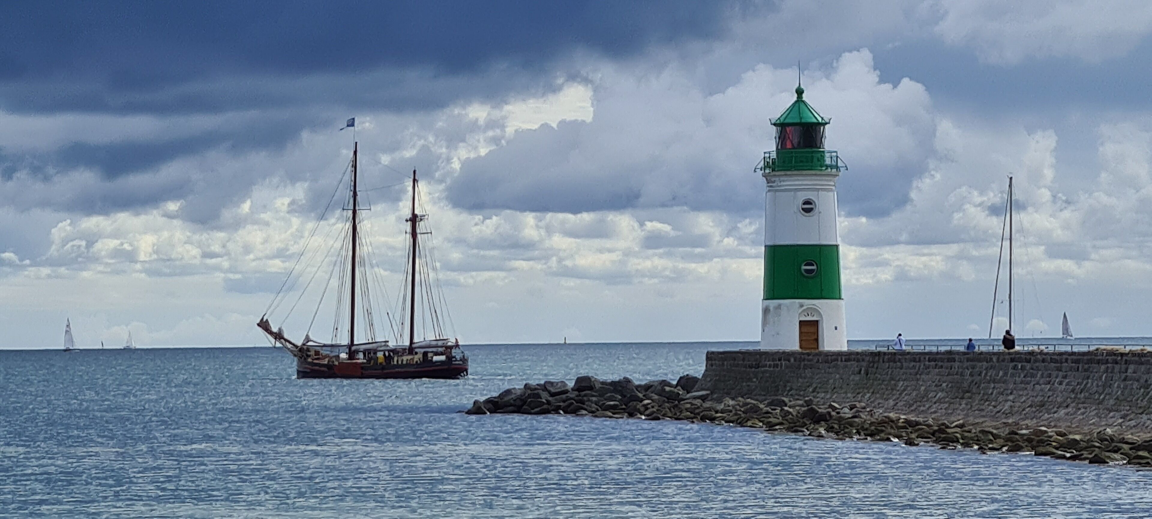 A lighthouse by the sea with a ship in the background.