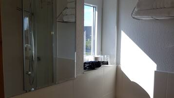 Une salle de bain équipée d’un lavabo, de toilettes et d’une douche. Une fenêtre laisse entrer la lumière naturelle et un porte-serviettes est fixé au mur.