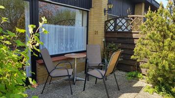A patio with two chairs and a table, a window with lace curtains, and a wooden fence.