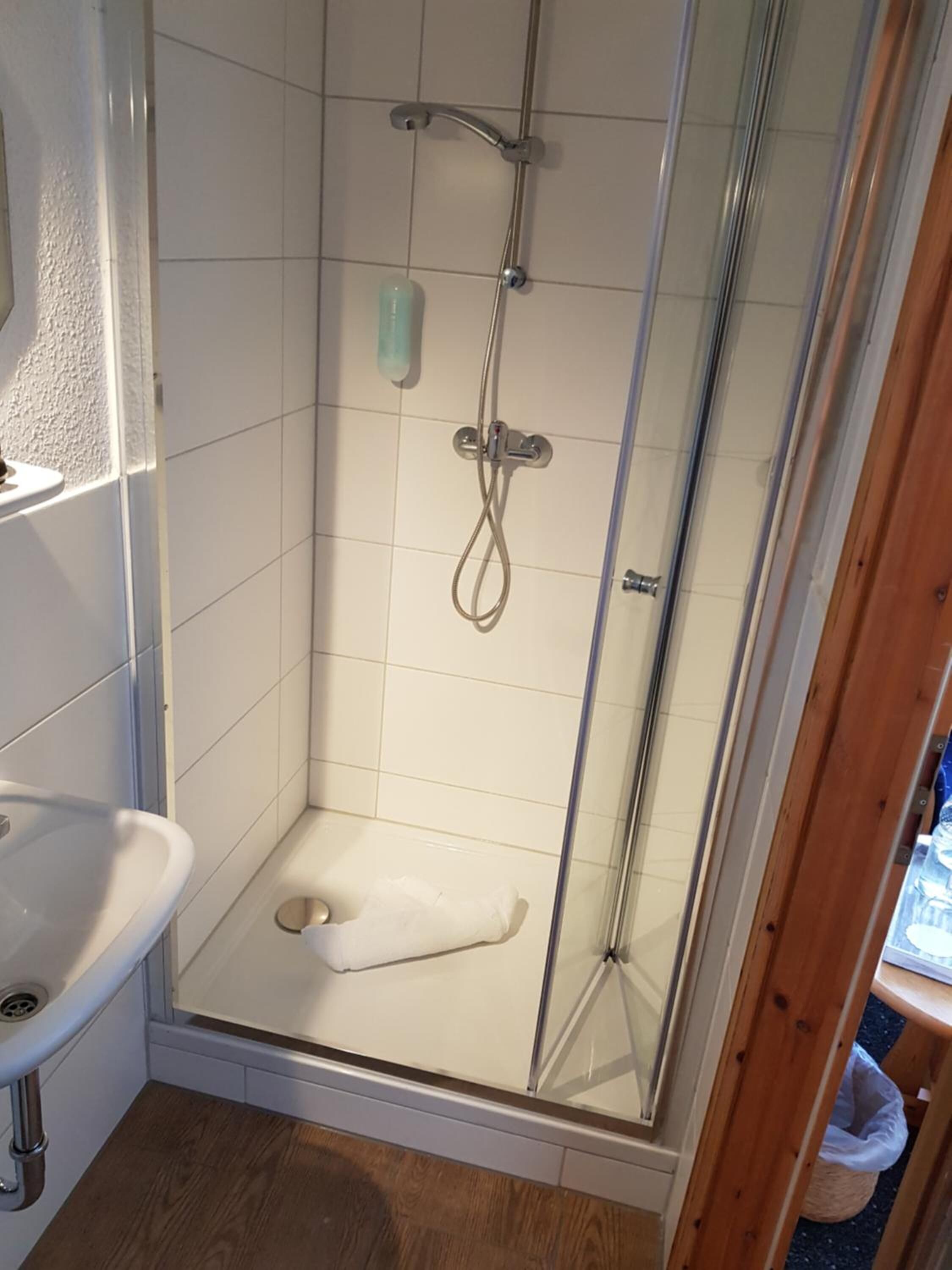 A shower with a glass door, a white sink, and a wooden floor.