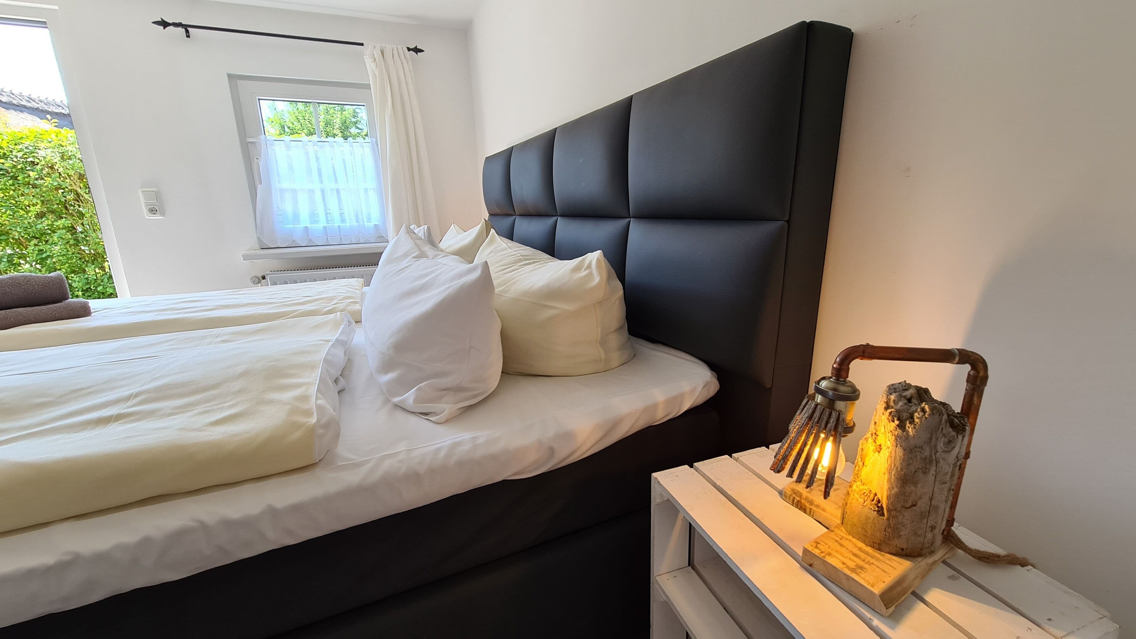 Un dormitorio con dos camas, ropa de cama blanca, cabecero negro y una lámpara de pared de estilo rústico.