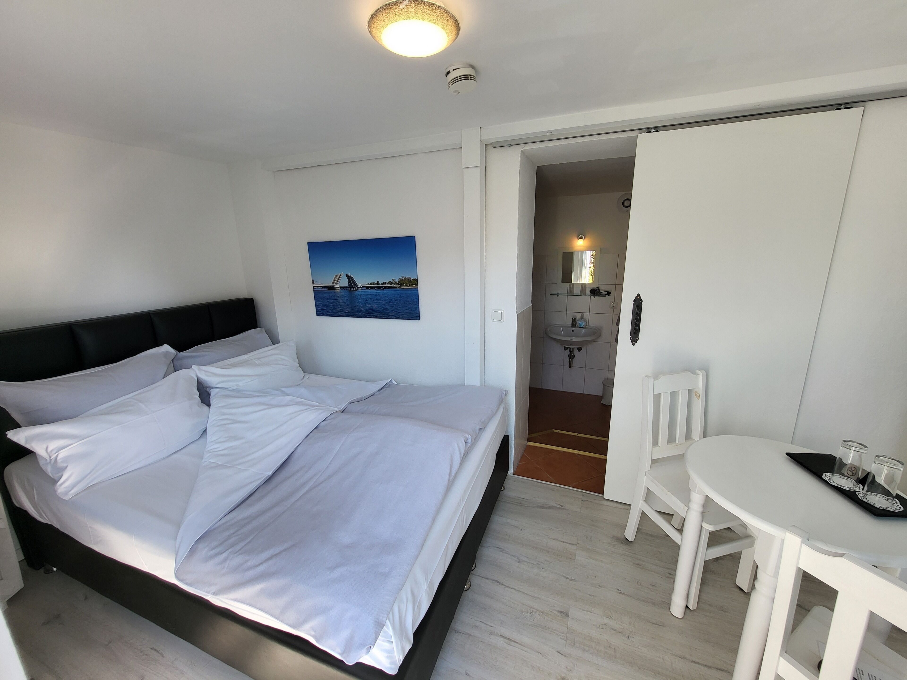 A bedroom with a bed, a white desk, and a bathroom visible through an open door.