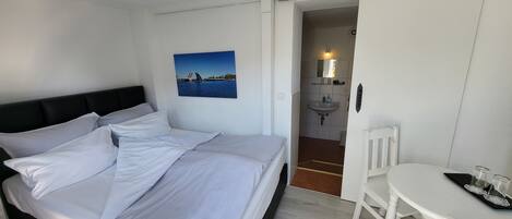 Un dormitorio con cama, un escritorio blanco y un baño visible a través de una puerta abierta.