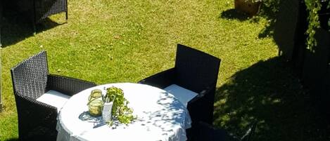 Un patio con mesas y sillas redondas, rodeado de vegetación y un seto.