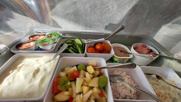 Een buffet met aangeduide gerechten, waaronder fruit yoghurt, komkommers, tomaten, vleessalade en een fruitsalade.