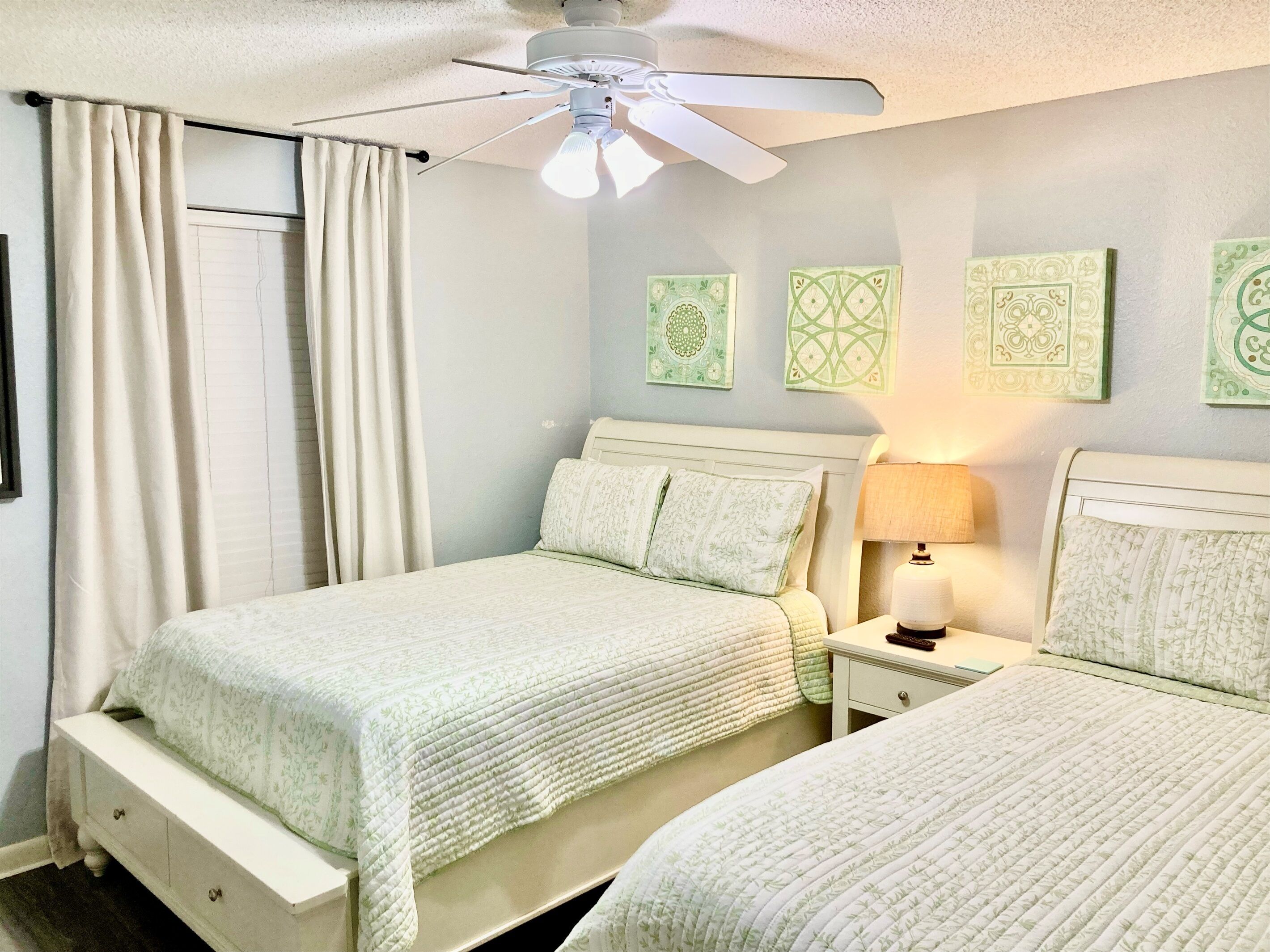 A bedroom with two beds, a ceiling fan, and a nightstand with a lamp.