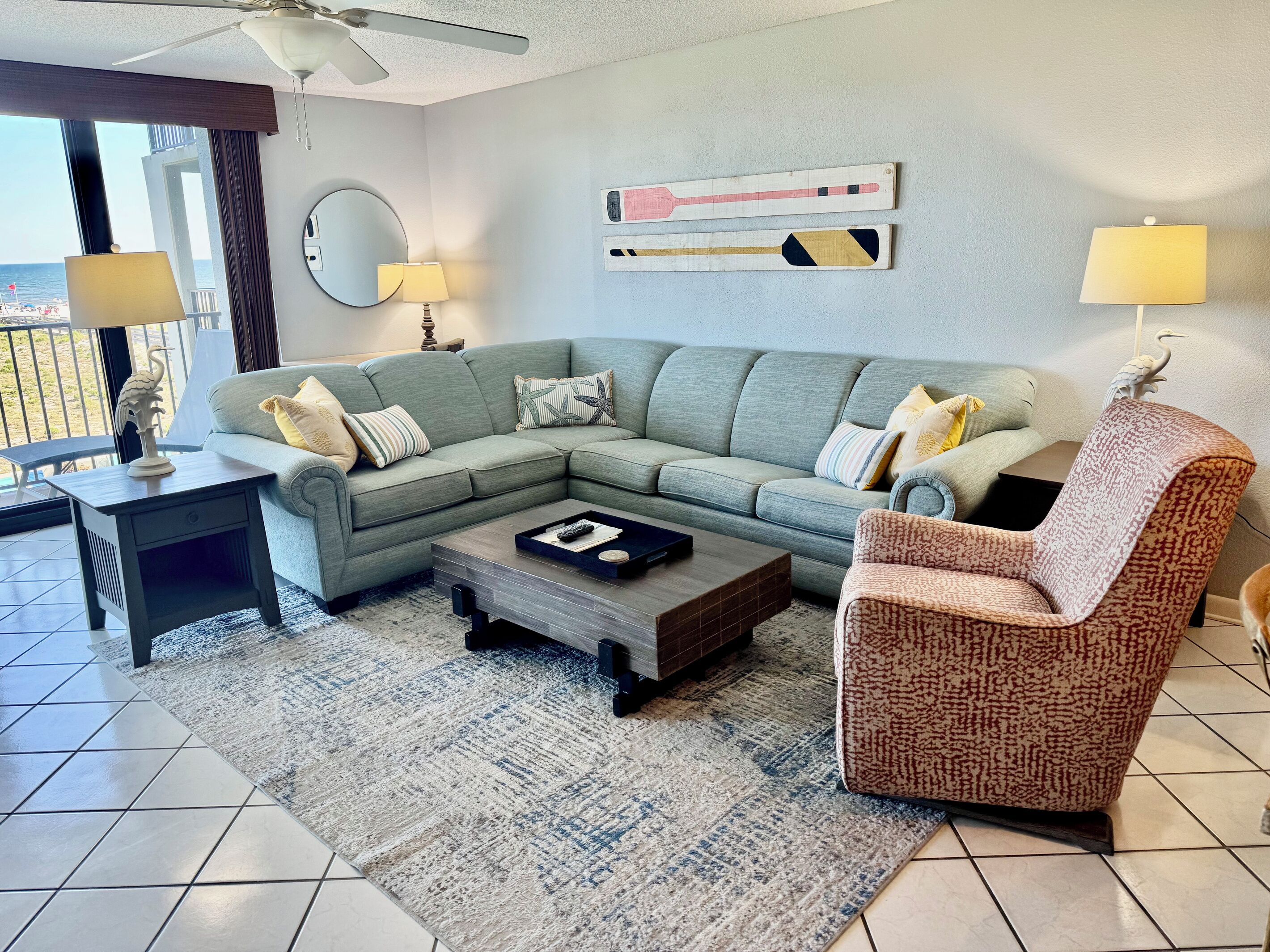 A living room with a sectional sofa, a patterned armchair, a coffee table, and a view of the ocean.
