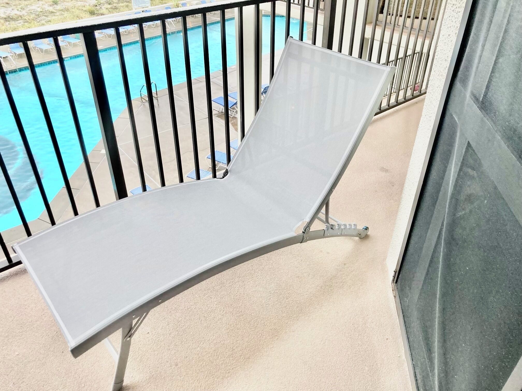 A balcony with a metal chair and a pool in the background.