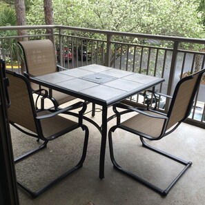 A balcony with a table and chairs, a railing, and a view of trees and parked cars. - Ocean One 306 - Oceanside prime beach location, walk to shops,dining, remodeled (Hilton Head Island)