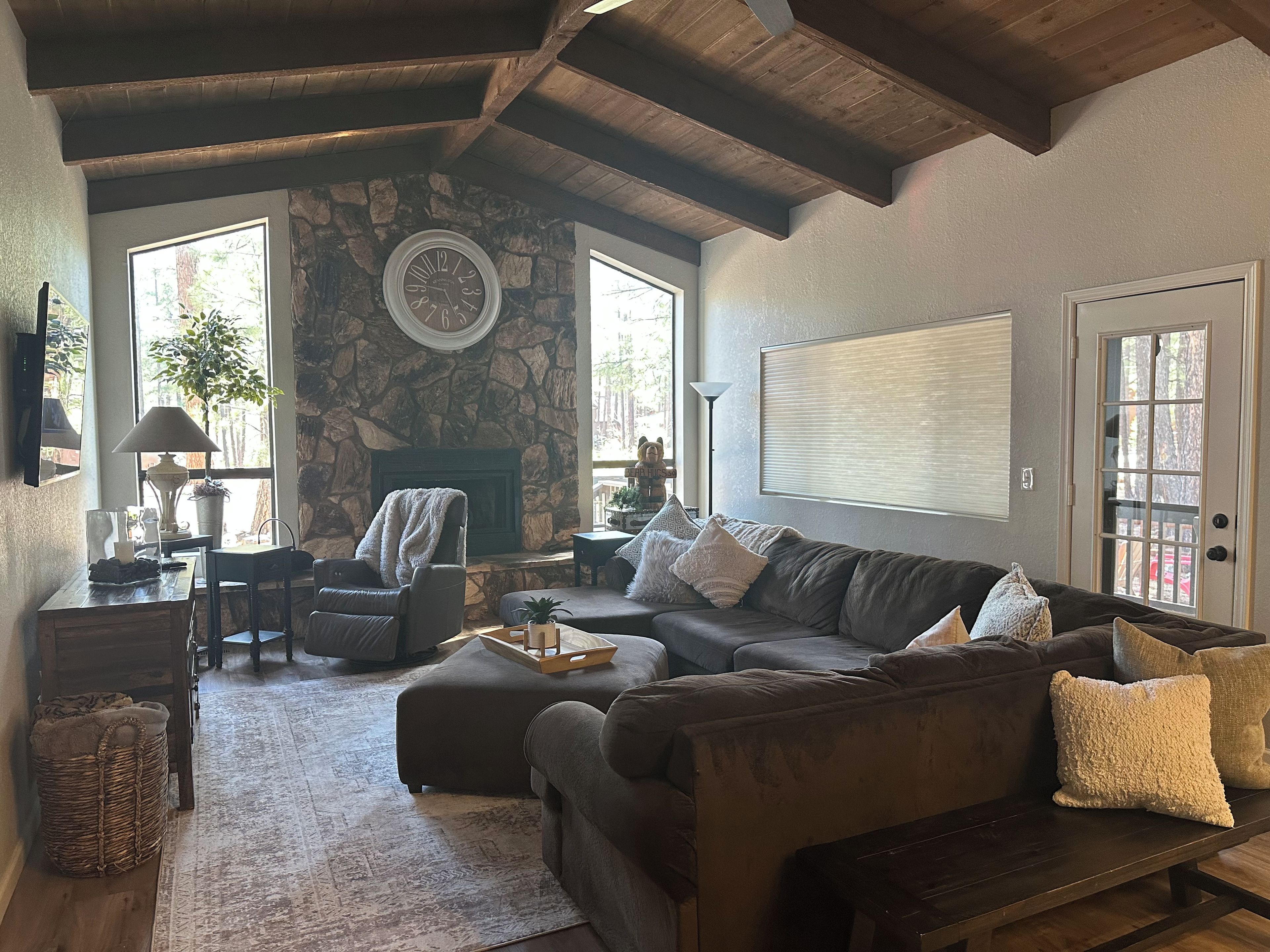 A cozy living room with a stone fireplace, a large clock, and a comfortable seating area.