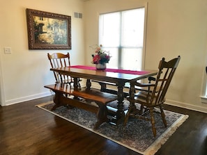 Un coin repas avec une table en bois, quatre chaises, un set de table rouge et un vase avec des fleurs.