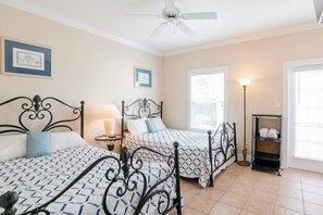 A hotel room with two beds, a ceiling fan, a lamp, a window with blinds, and a shelf with towels. - Purple Parrot Condo Near Beach with Pool (Pensacola)