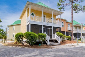 A two-story house with a porch, a green roof, and a small front yard with trimmed bushes. - Purple Parrot Condo Near Beach with Pool (Pensacola)