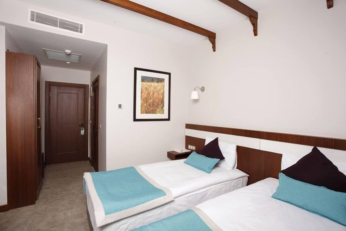 A hotel room with two beds, a wooden ceiling, a framed picture on the wall, and a nightstand.