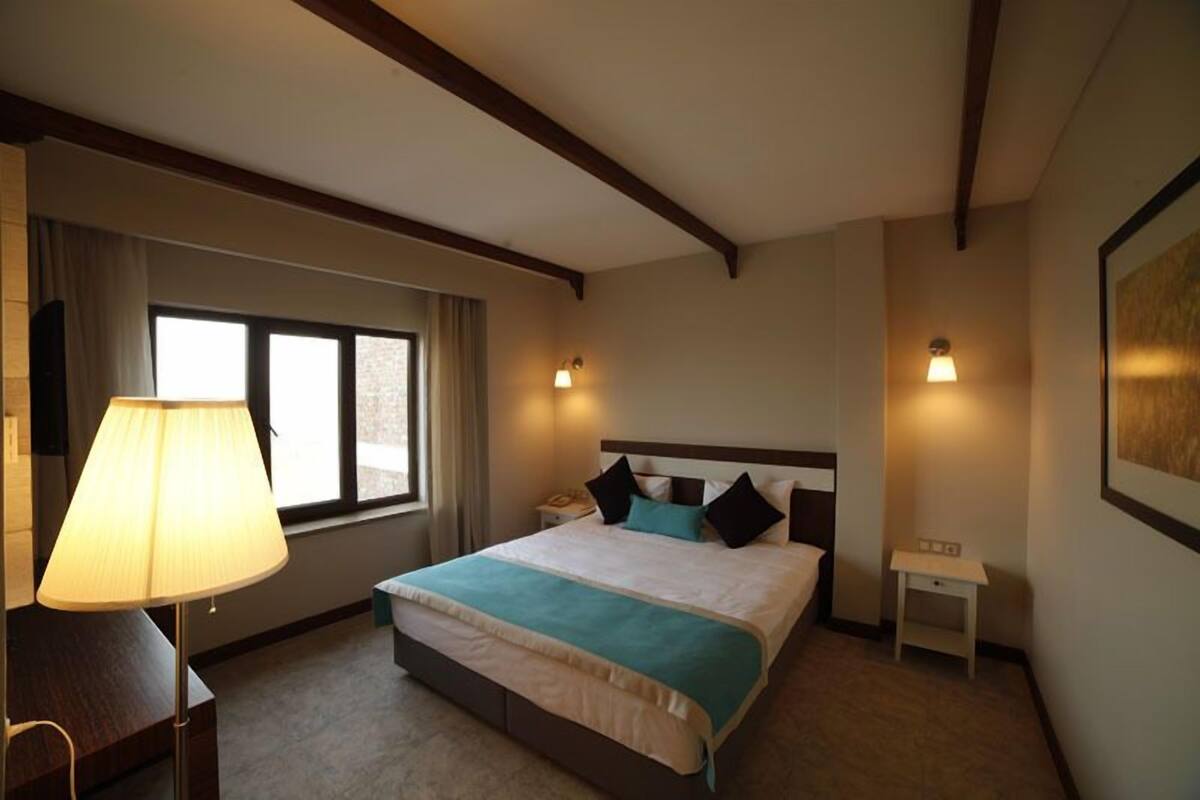 A hotel room with a bed, bedside lamp, nightstand, and a window with curtains.