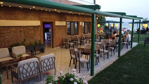 Un patio al aire libre con muros de ladrillo, varias mesas y sillas, y una zona de estar cubierta.