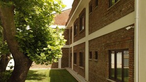 Un patio con un edificio de ladrillo, un árbol y un césped bien cuidado.