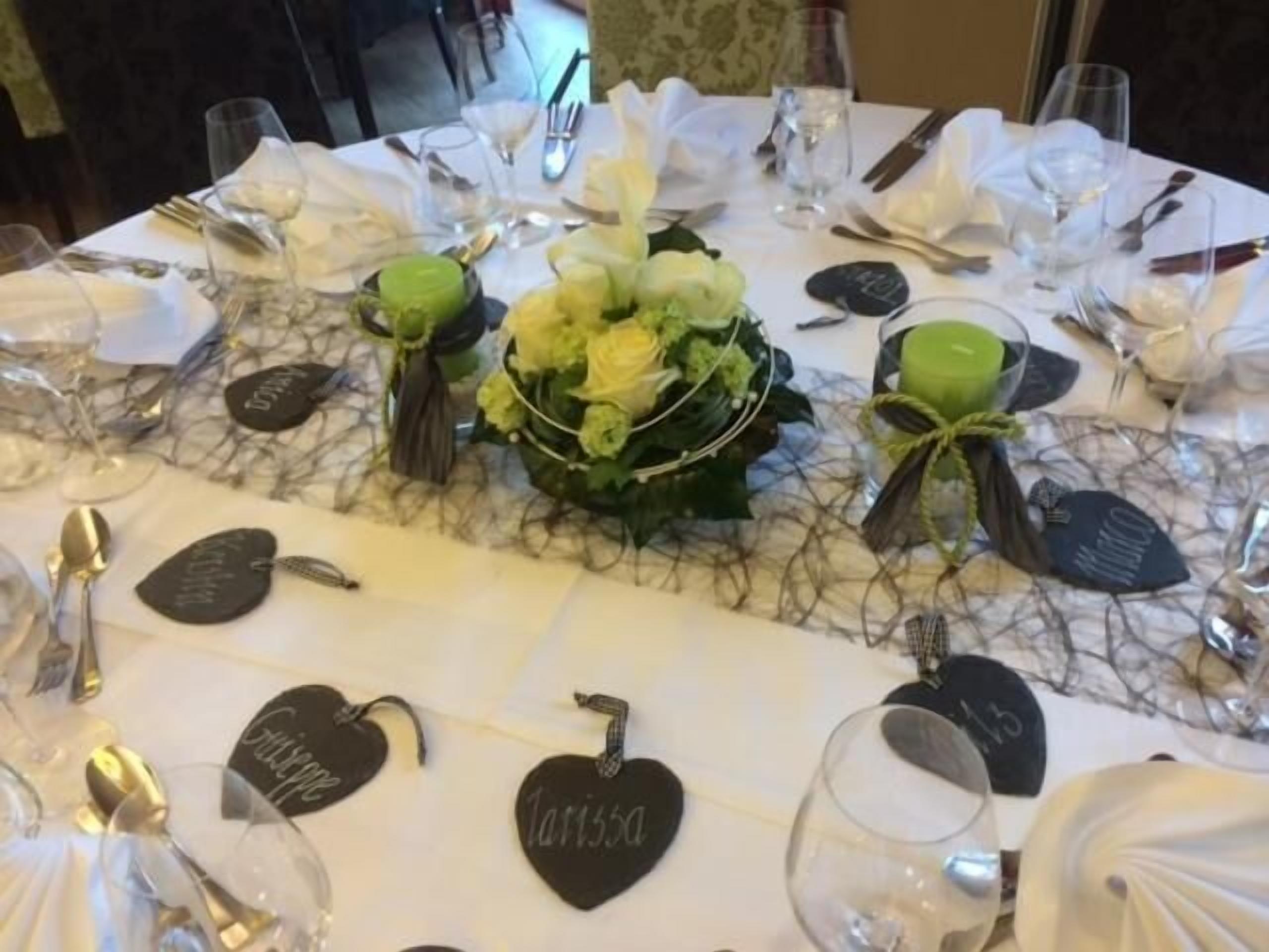 Ein gedeckter Tisch mit herzförmigen Namensschildern, einem Blumenarrangement als Mittelpunkt und einer Tischdecke aus Marmor.