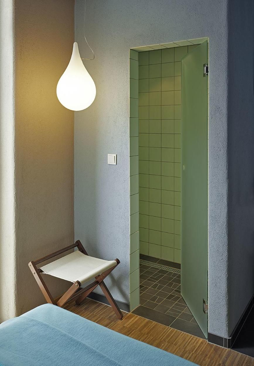 Ein Zimmer mit einem Bett, einer Hängeleuchte, einer grünen Tür und einem kleinen Holzstuhl.