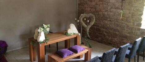 A room with a stone wall, a wooden bench, a table with a vase and flowers, and heart-shaped decorations.
