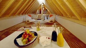 Een zolderkamer met een hoog houten plafond, een tafel gedekt met fruit, glazen en een kan sap.