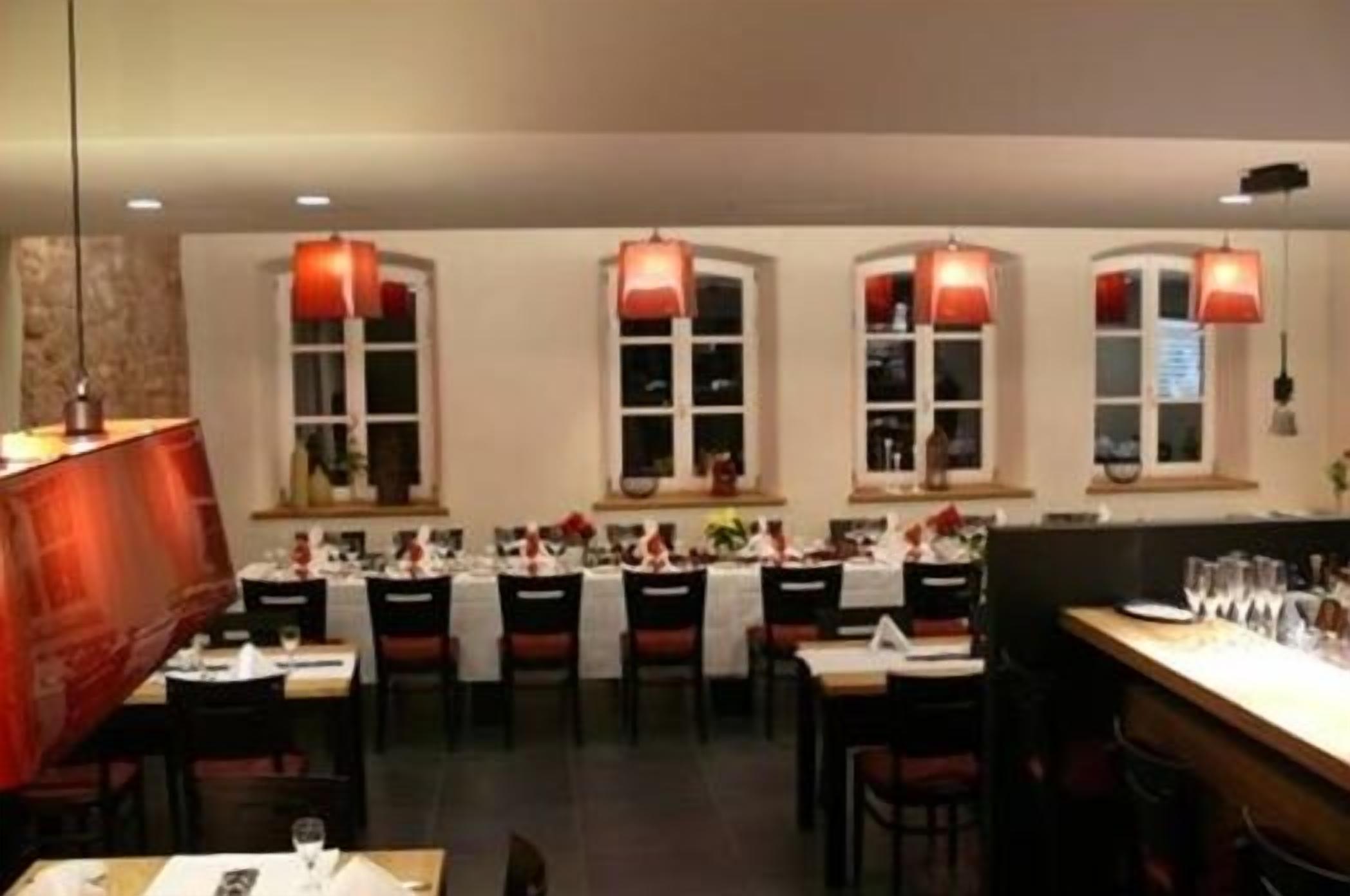 Un restaurante con varias mesas y sillas, lámparas colgantes rojas y una zona de bar.