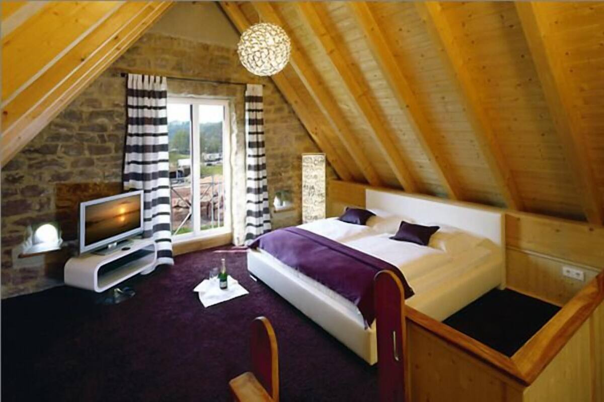 Ein Schlafzimmer mit Bett, Fernseher, Fenster mit Vorhängen und einer Steinwand.