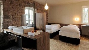 Een moderne hotelkamer met een stenen muur, een groot wastafel, twee bedden en een bureau.