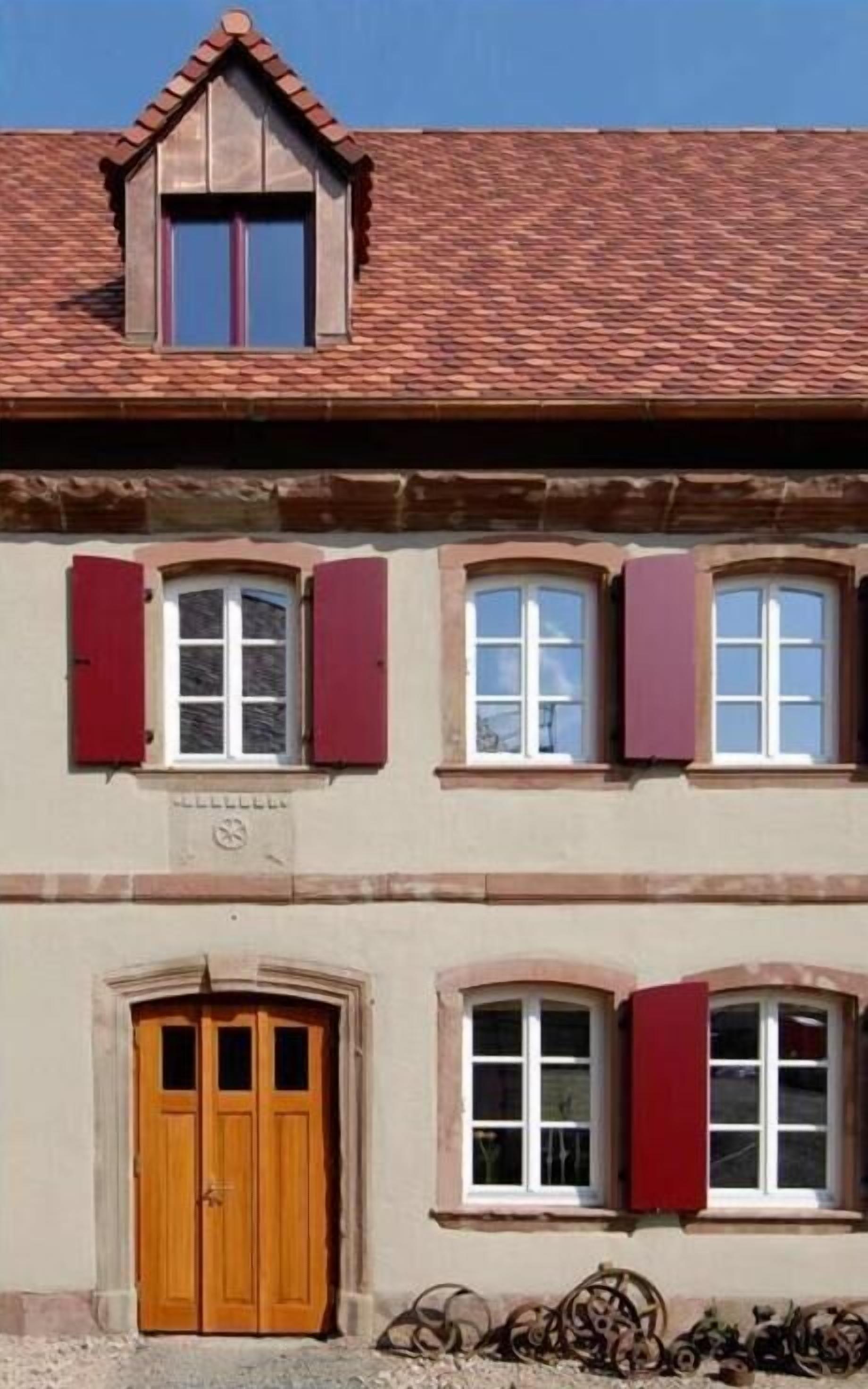 A building with a pitched roof, multiple windows with shutters, and a wooden door.