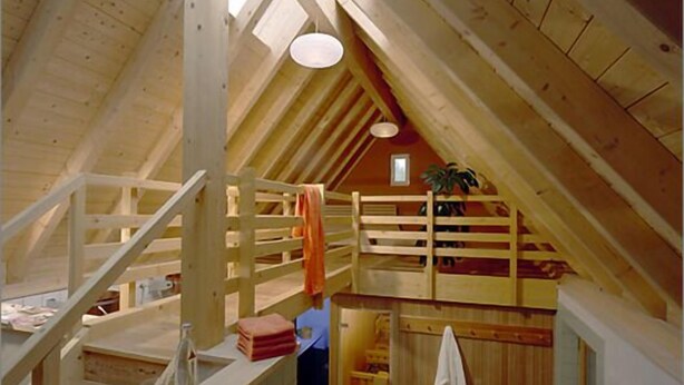 Een zolderkamer met hoge plafonds, een houten trap, een klein badkamertje en uitzicht door de dakramen.