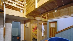Een sauna met houten plafond, glazen deur en een blauw bubbelbad.