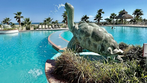 Una piscina con una gran escultura de elefante, palmeras y vista al océano.