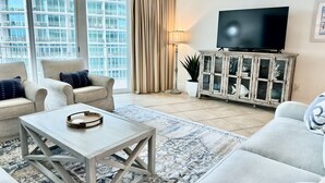 Una sala de estar con sofá, sillón, mesa de centro, televisor y un mueble con adornos.