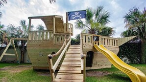 Una estructura de juego de madera con temática pirata que incluye un tobogán y un puente de cuerda.