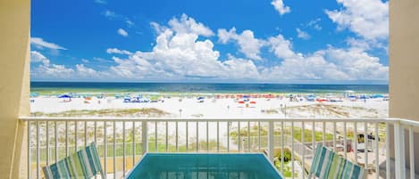 A balcony with a view of a beach, a pool table, and striped chairs.