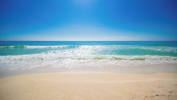 A beach with clear blue water and a sandy shore.