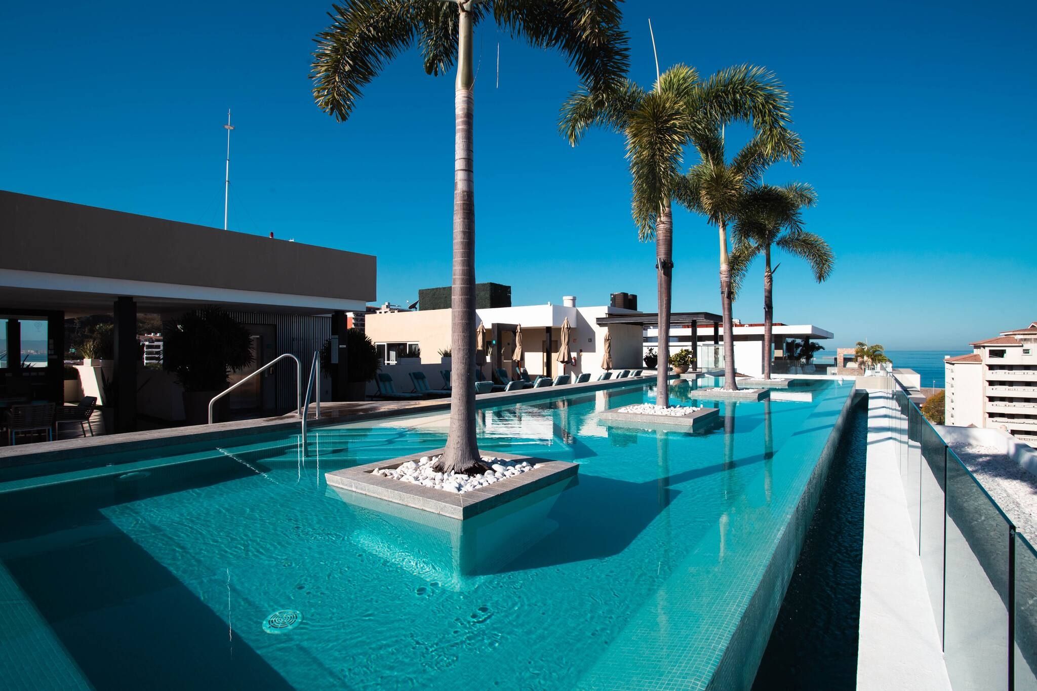 A pool area with clear blue water, palm trees, and modern buildings.