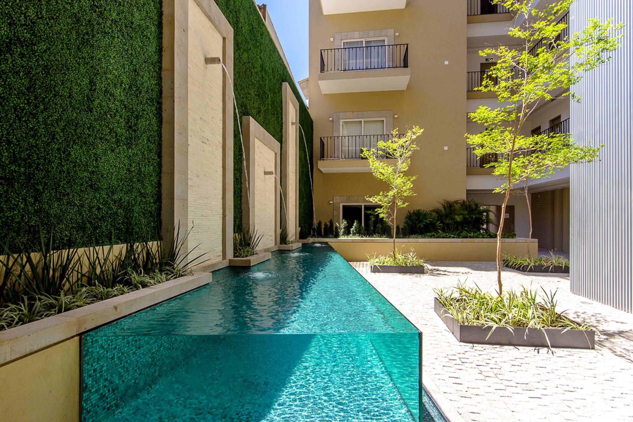 A swimming pool with a green wall and a building with balconies.