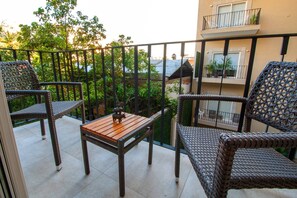 A balcony with wicker furniture, a table, and a view of a building with balconies.
