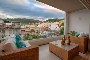 A balcony with wicker furniture, a view of a cityscape, and a clear sky.